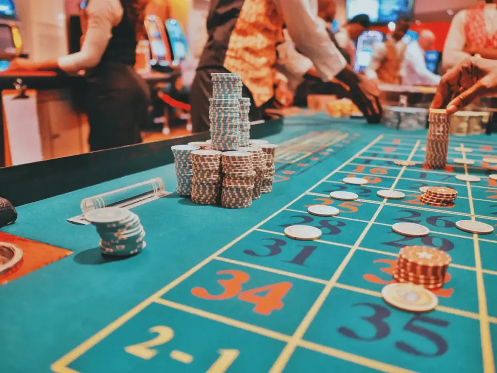 Photo of stacks of casino chips on a roulette table with players and dealers in the background